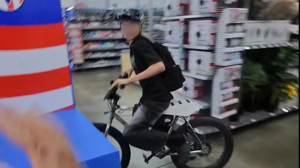A juvenile male riding an e-bike down a Walmart aisle, with store shelves and products blurred in the background.
