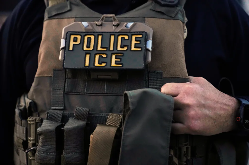 Close-up of an Immigration and Customs Enforcement (ICE) agent wearing a tactical vest with a 