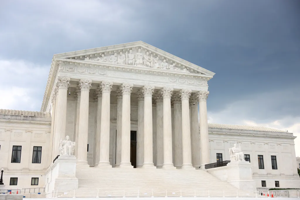 The United States Supreme Court building, featuring a white neoclassical facade with Corinthian columns and statuary, under a cloudy sky.