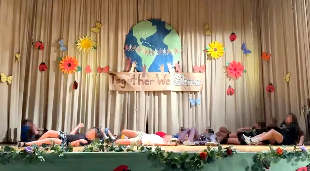 Upper West Side elementary school children lie on the stage in a choreographed dance, with a backdrop of a globe and a banner that reads 
