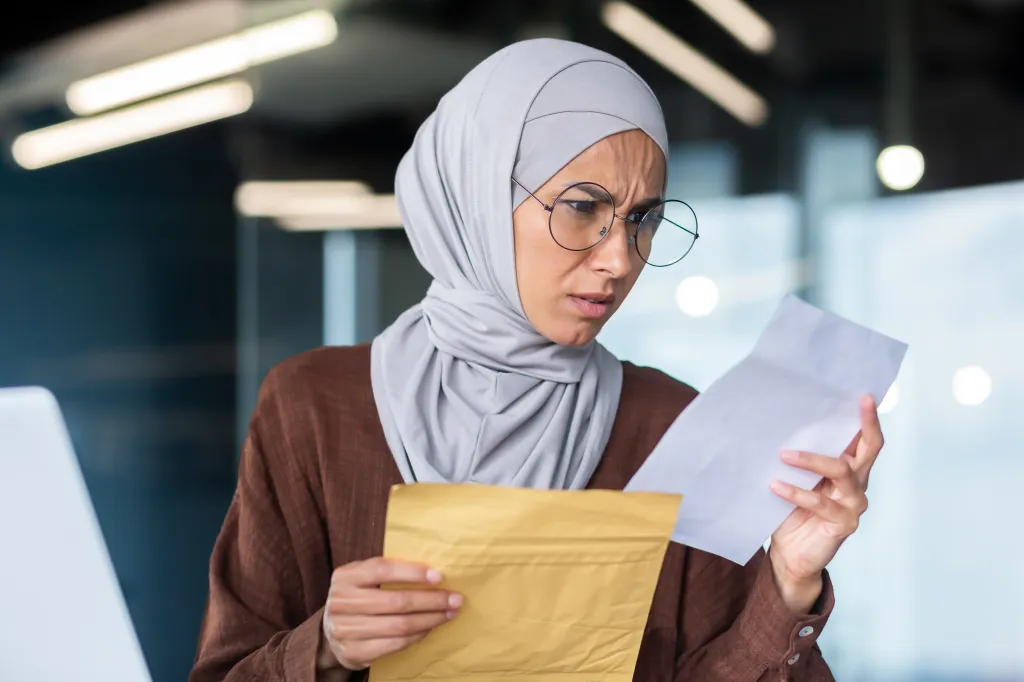 Upset business woman in a hijab and glasses reading a letter.