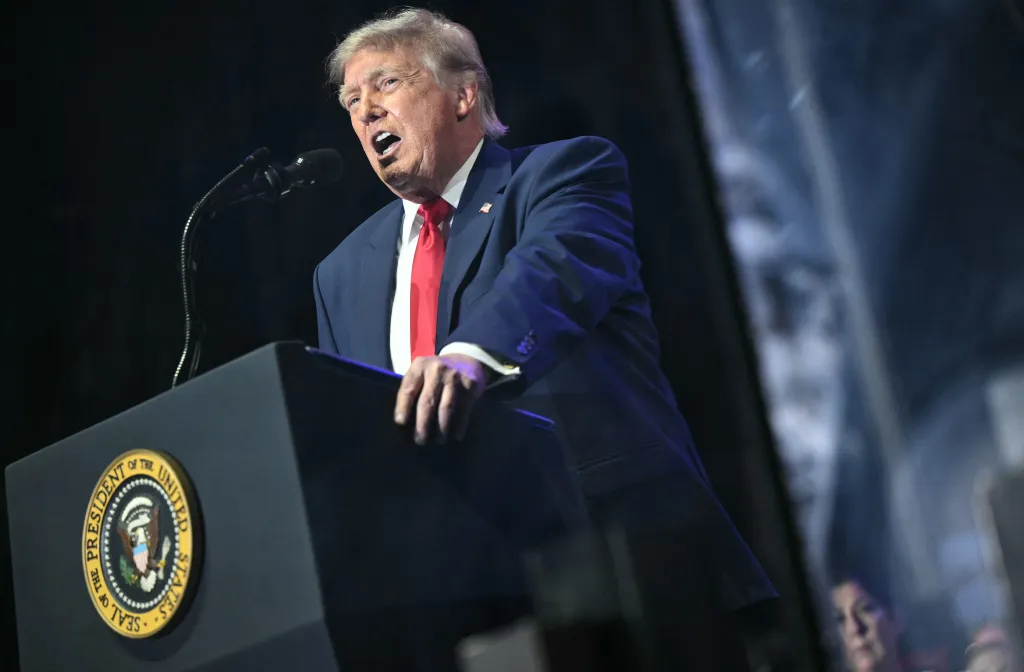 Donald Trump speaking at a podium with the Seal of the President of the United States.