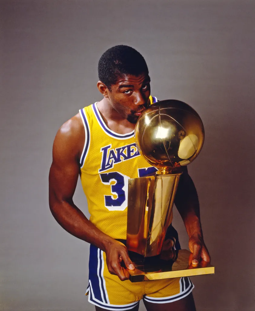 Magic Johnson in his Lakers jersey, holding and kissing a gold trophy.