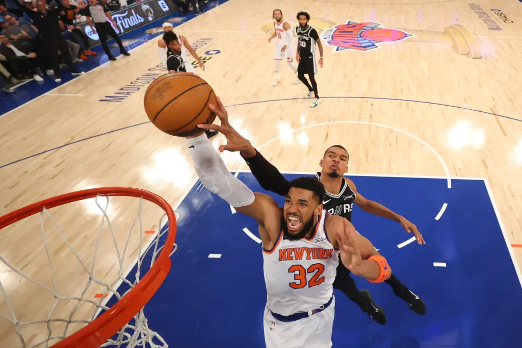 Karl-Anthony Towns of the New York Knicks attempts a shot while being fouled by Victor Wembanyama of the San Antonio Spurs during Game Four of the 2026 NBA Finals.