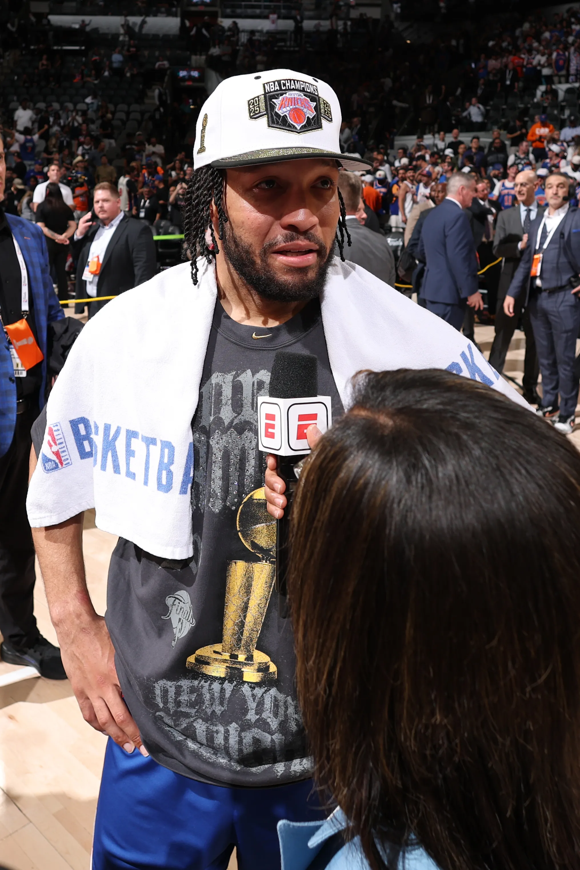 Jalen Brunson wearing an NBA Champions hat and a T-shirt with the trophy being interviewed.