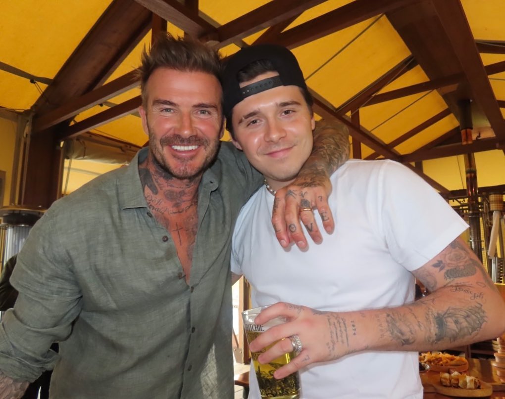 David Beckham smiling with his arm around Brooklyn Beckham.