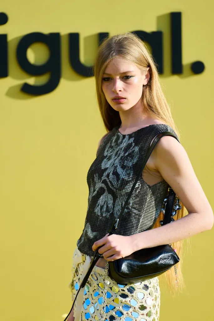 Vivian Jenna Wilson poses in a Desigual outfit against a yellow backdrop with the brand's logo.