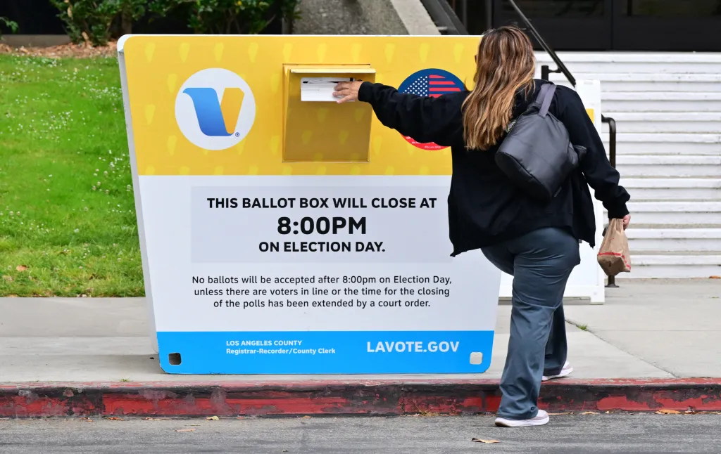 A person casts their ballot into a yellow and white ballot drop box in Los Angeles County.