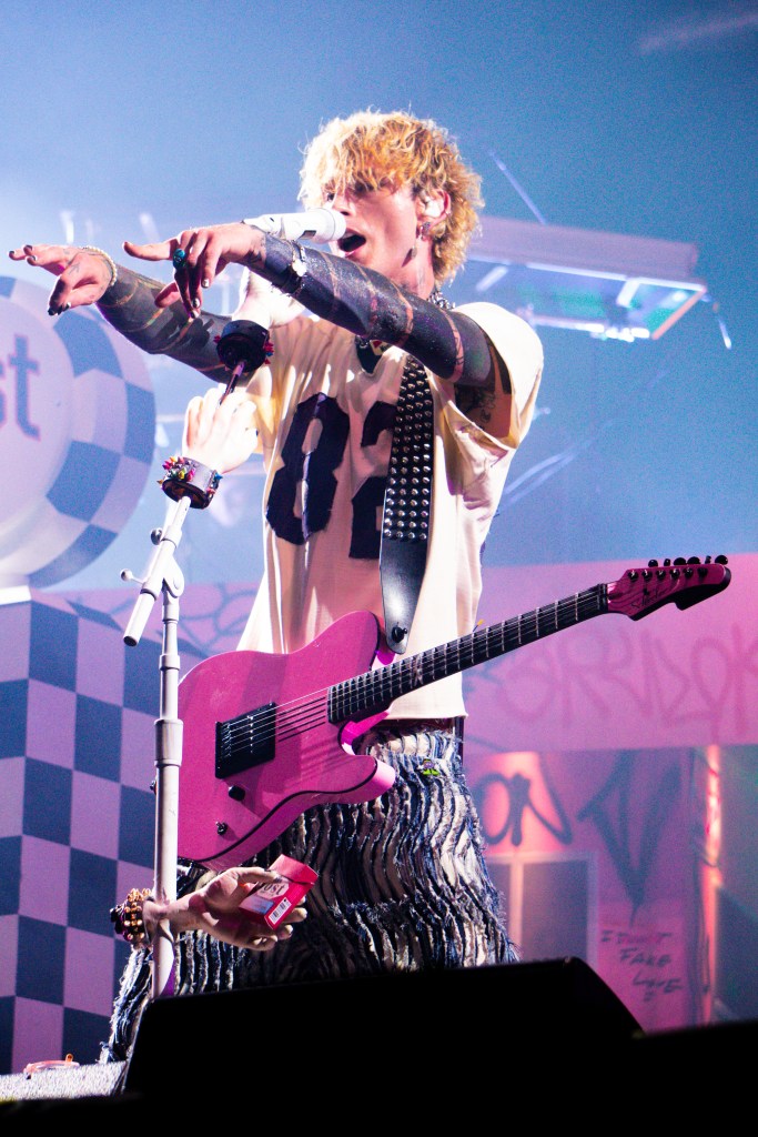 Machine Gun Kelly performing on stage with a pink guitar and microphone.