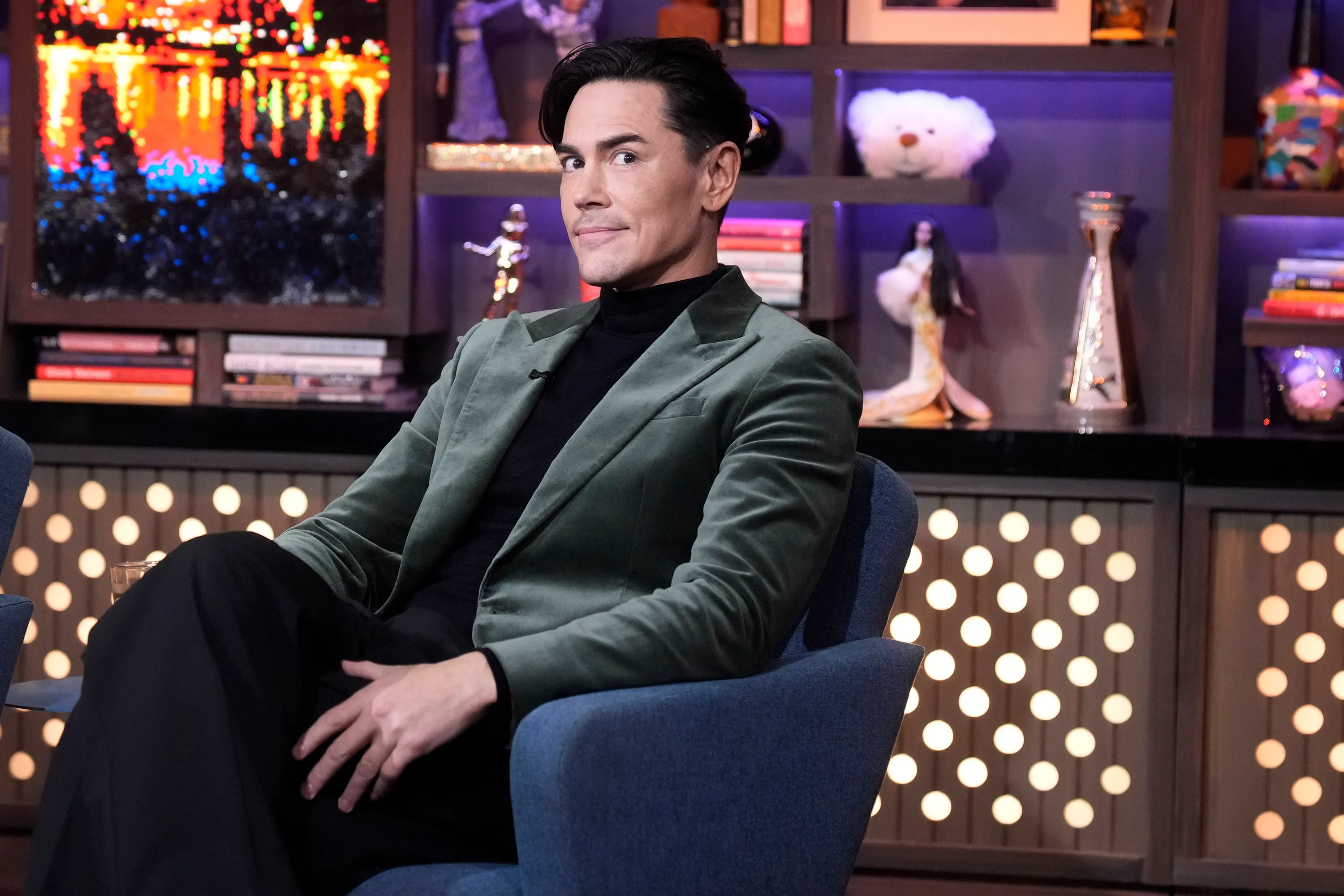 Tom Sandoval in a green velvet blazer sits in a blue chair, looking forward with a slight smile.