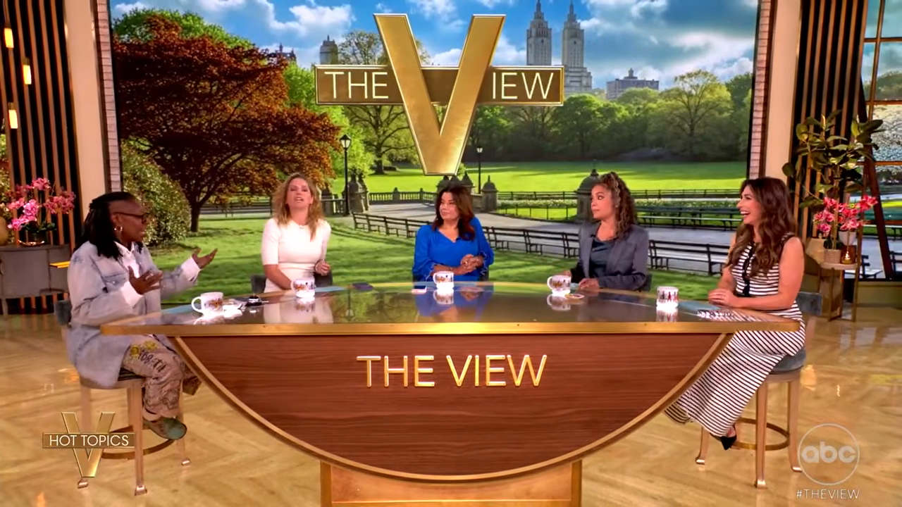 Five women sit at a curved desk with 