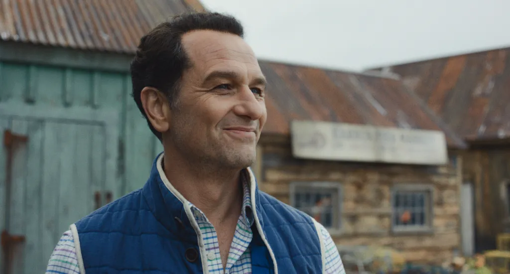 Matthew Rhys smiling with a rustic background.