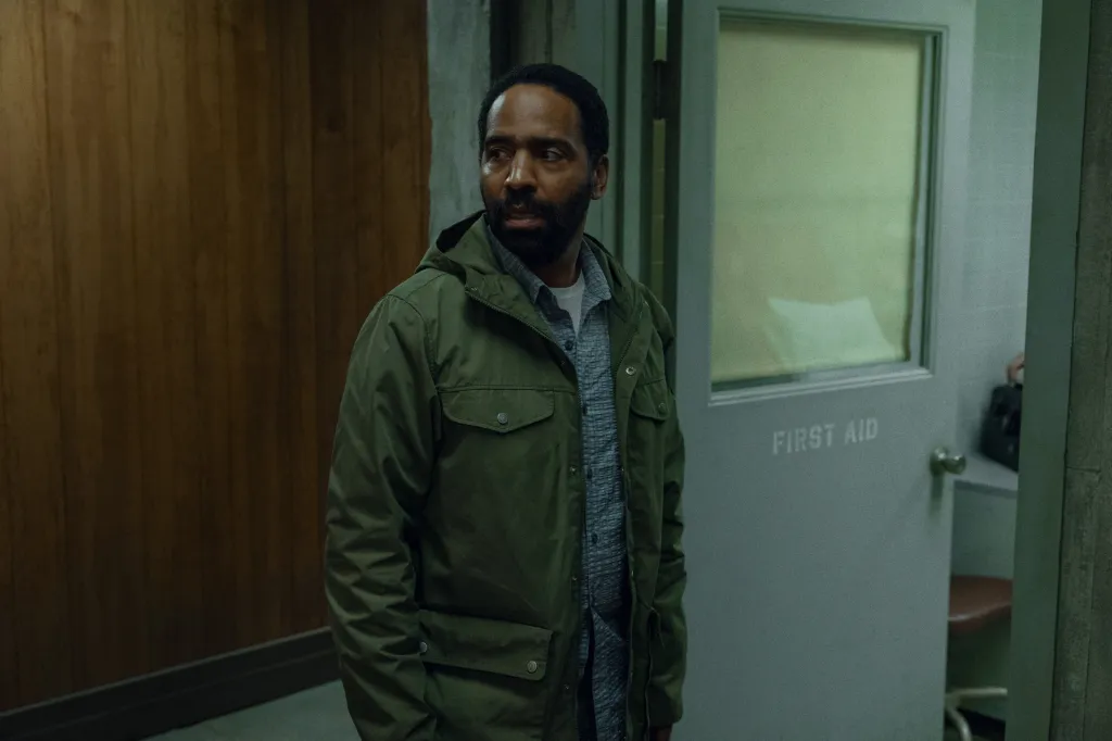 Man in an olive green jacket looks to the right of the frame, next to a 