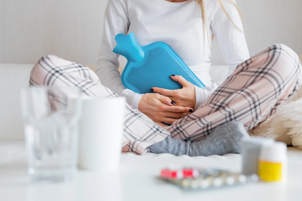 Woman sitting on a couch with a hot water bottle on her stomach.