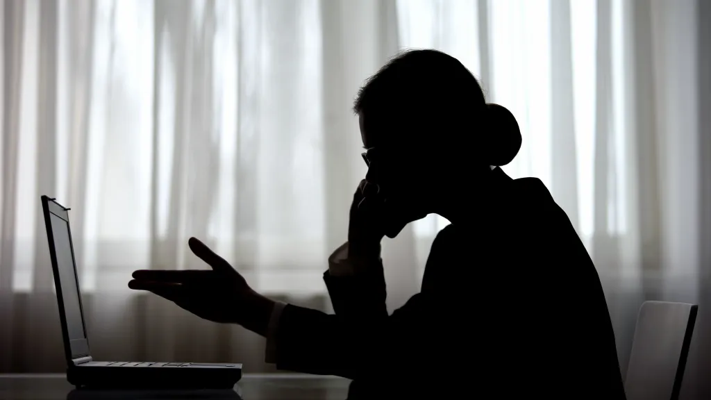 Silhouette of a businesswoman on the phone, looking at a laptop with an open hand gesture.