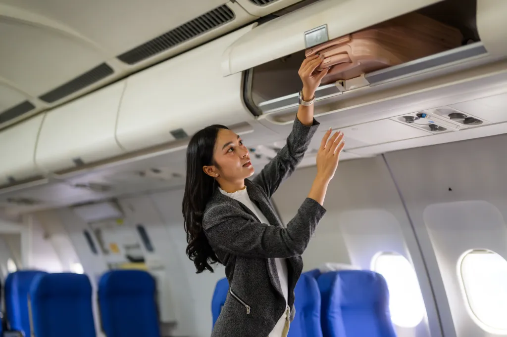 A woman putting luggage into an airplane's overhead compartment.