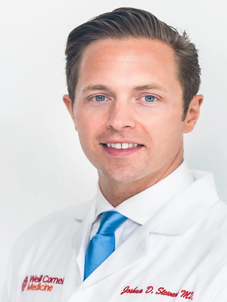 Headshot of Dr. Joshua Stewart smiling while wearing a white lab coat and blue tie.