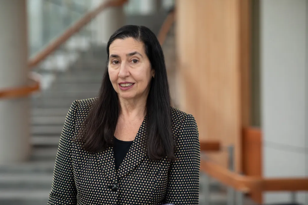 Dr. Judi Chervenak, a woman with long dark hair, smiles at the camera while wearing a black and gold polka dot jacket.