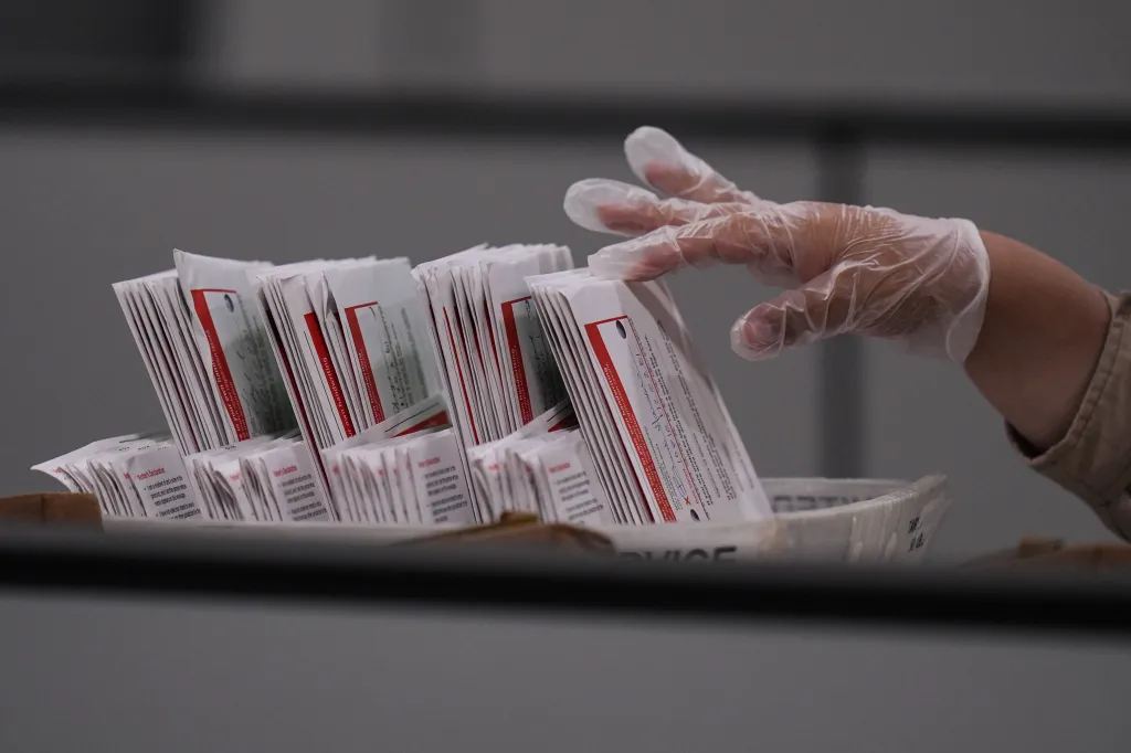 A worker wearing a clear glove inspects ballots in a bin.