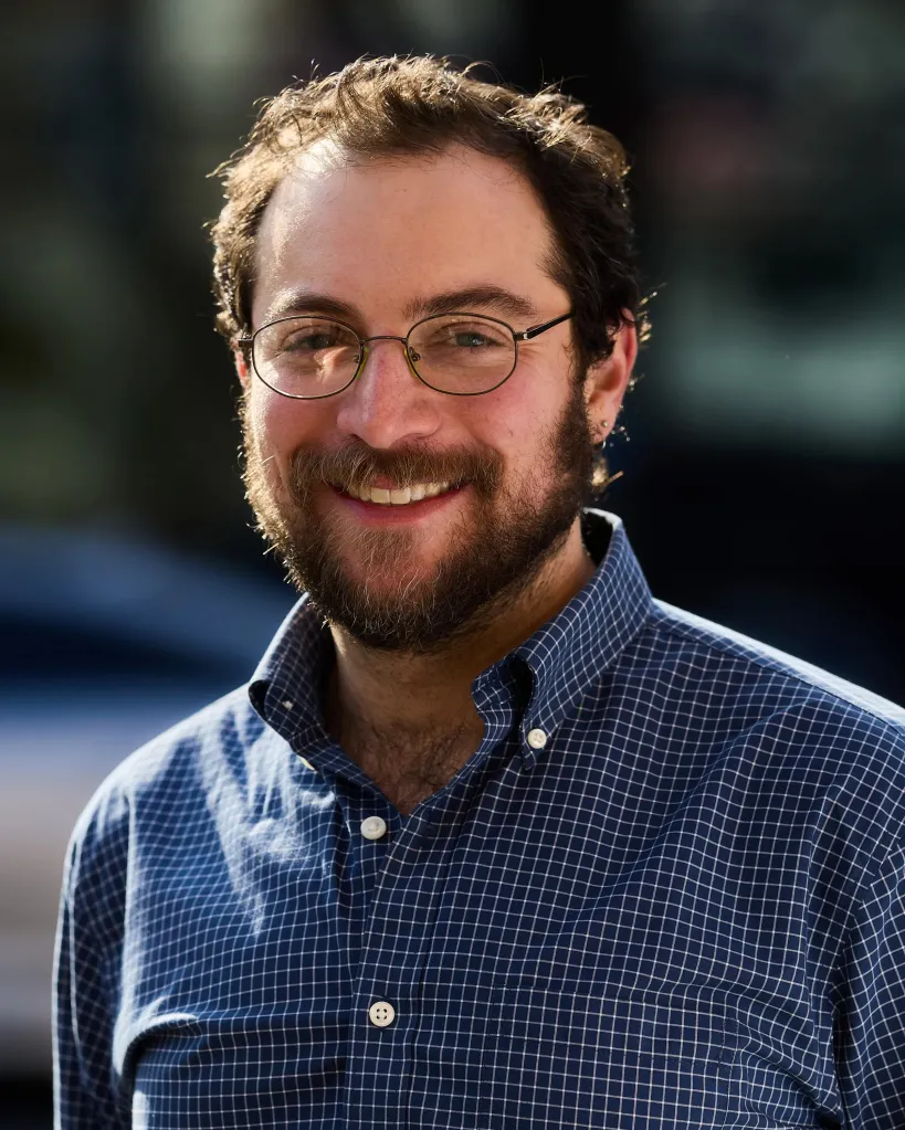 David Orkin, a man with a beard and glasses, smiles while wearing a plaid shirt.