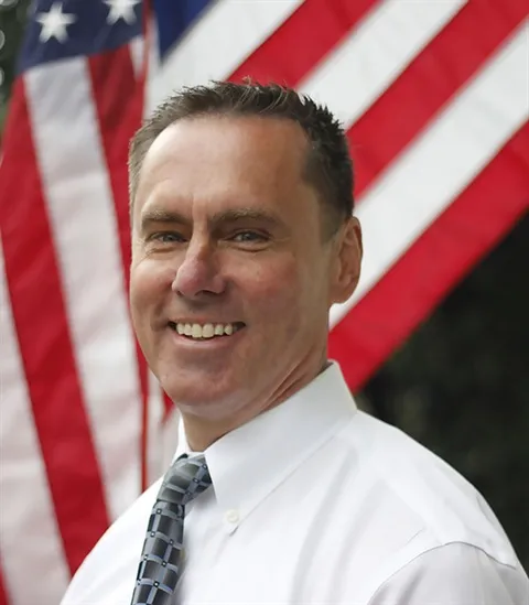 Vern Pierson, District Attorney, smiling in front of an American flag.