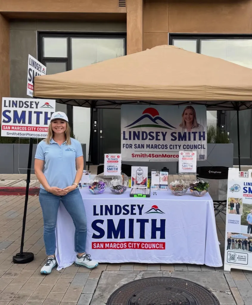 Lindsey Smith campaigning for San Marcos City Council next to her campaign booth.