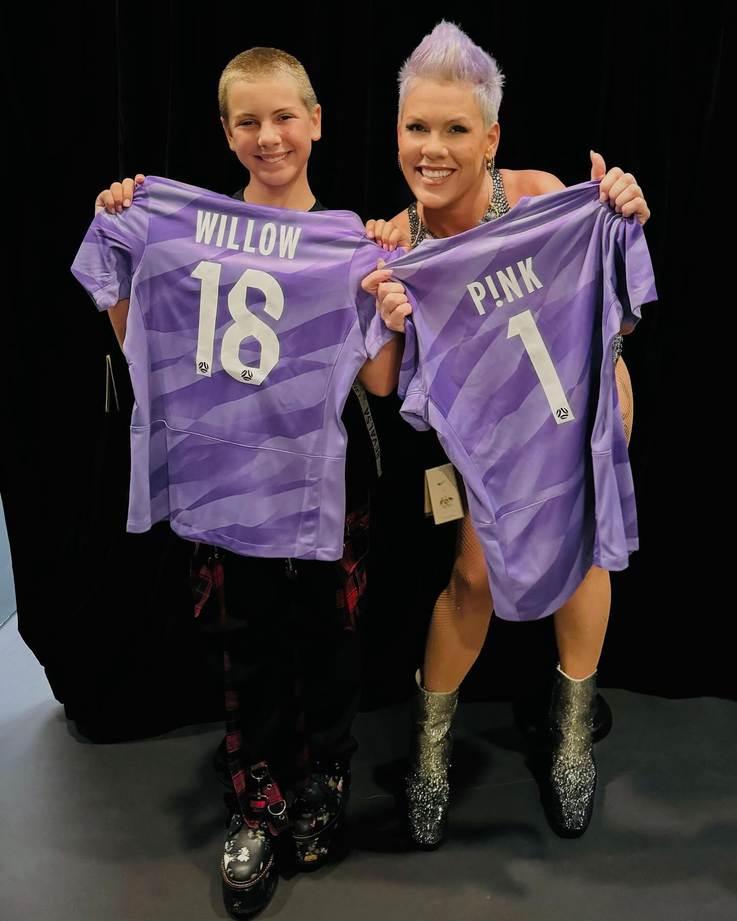Pink and her daughter Willow holding up purple soccer jerseys with their names and numbers.