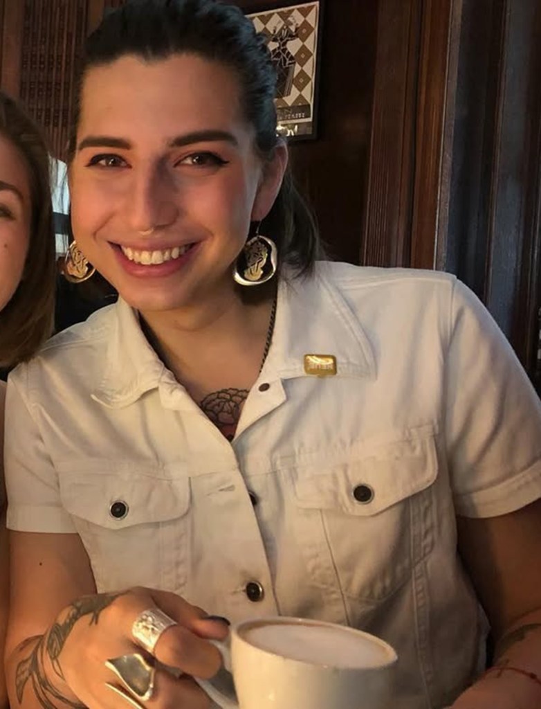 Persephone Ambriz-Squires, a trans Brooklyn photographer, smiling and holding a cup.