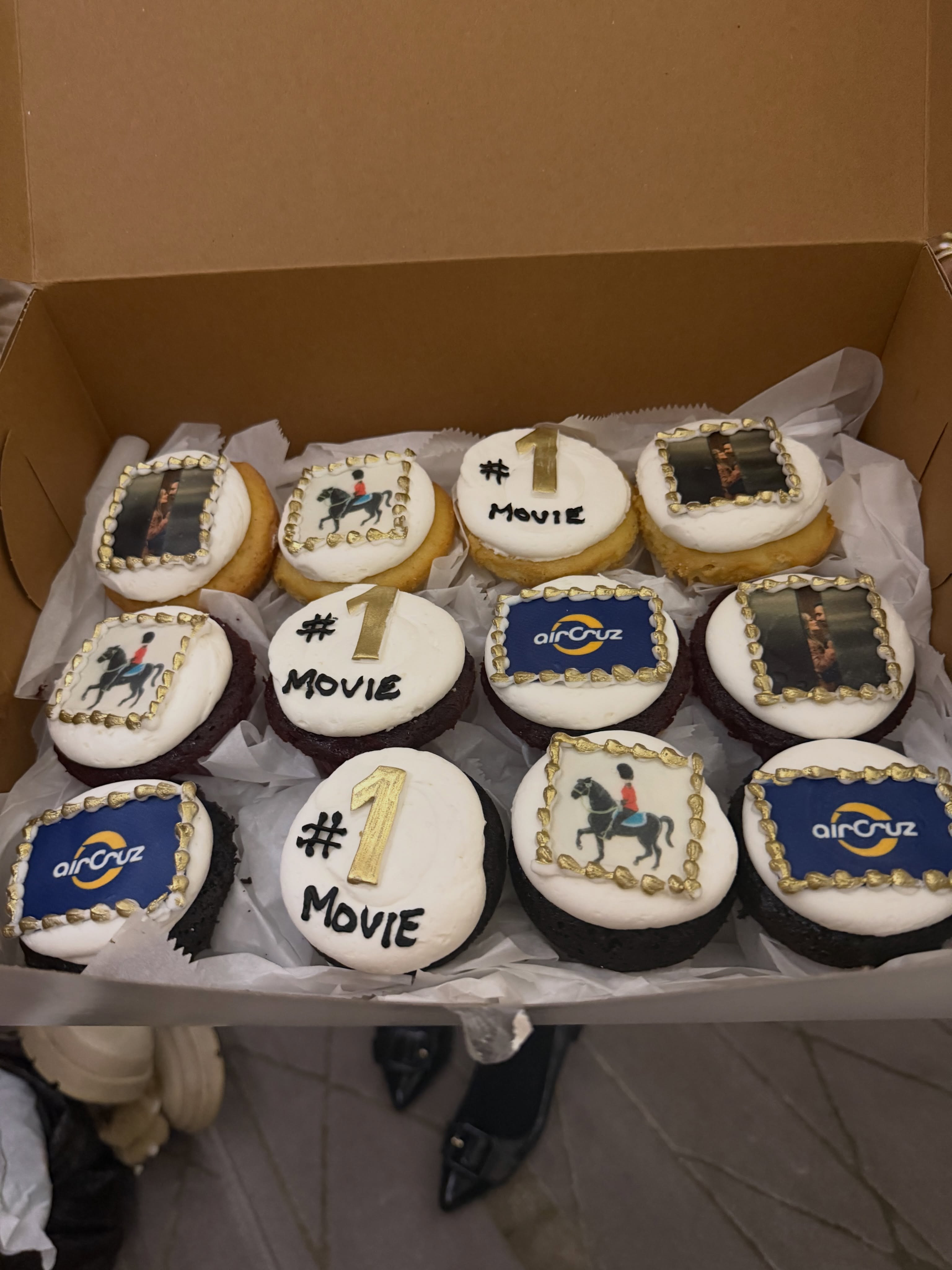 A box of cupcakes with varying images on their frosting: pictures of people, an 