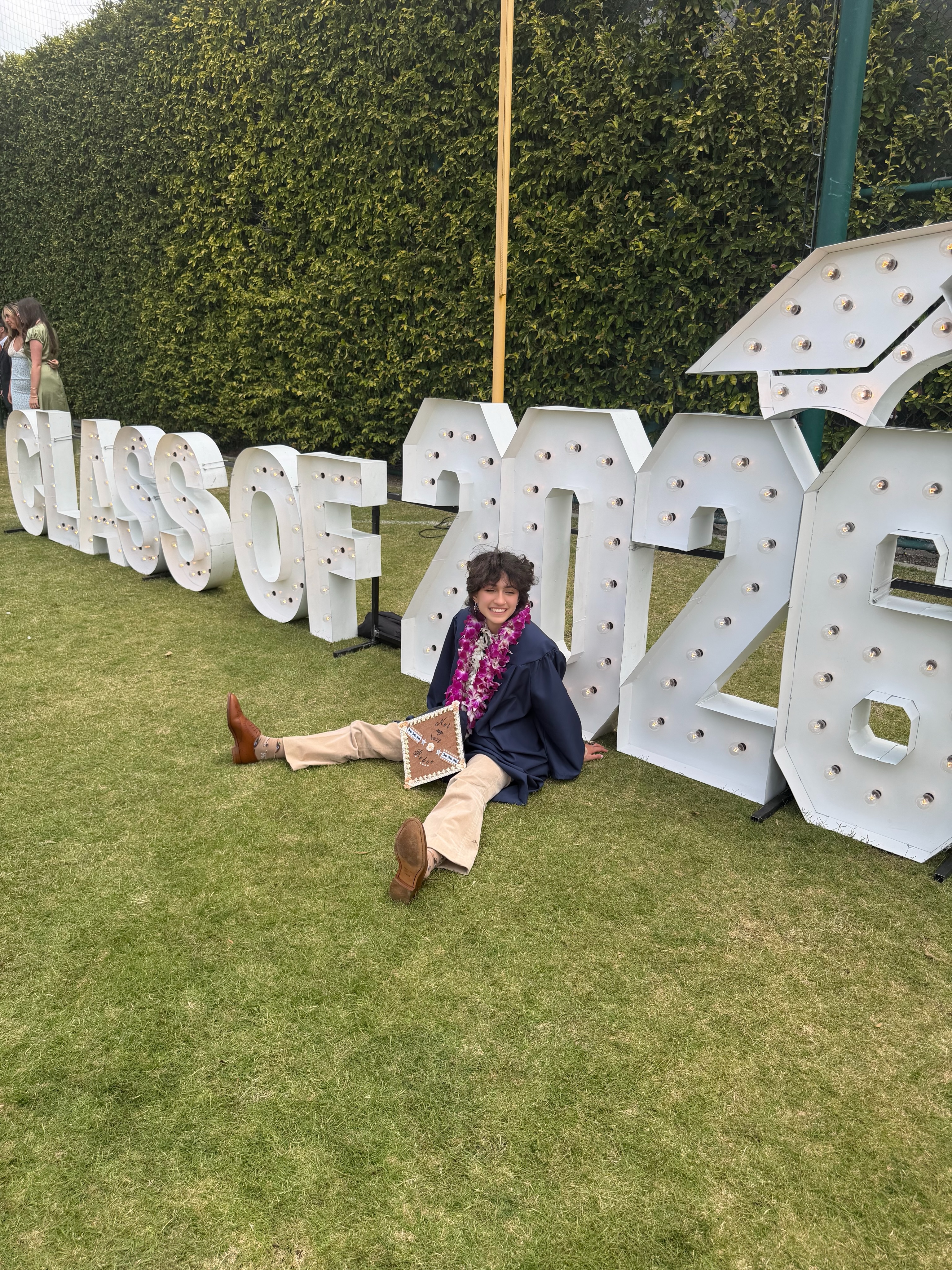 Oskar, in a graduation gown and lei, sits in front of a 