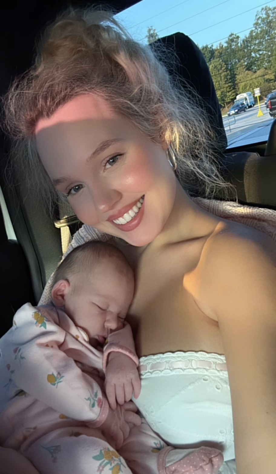 Estee Williams smiling and holding her sleeping baby daughter.