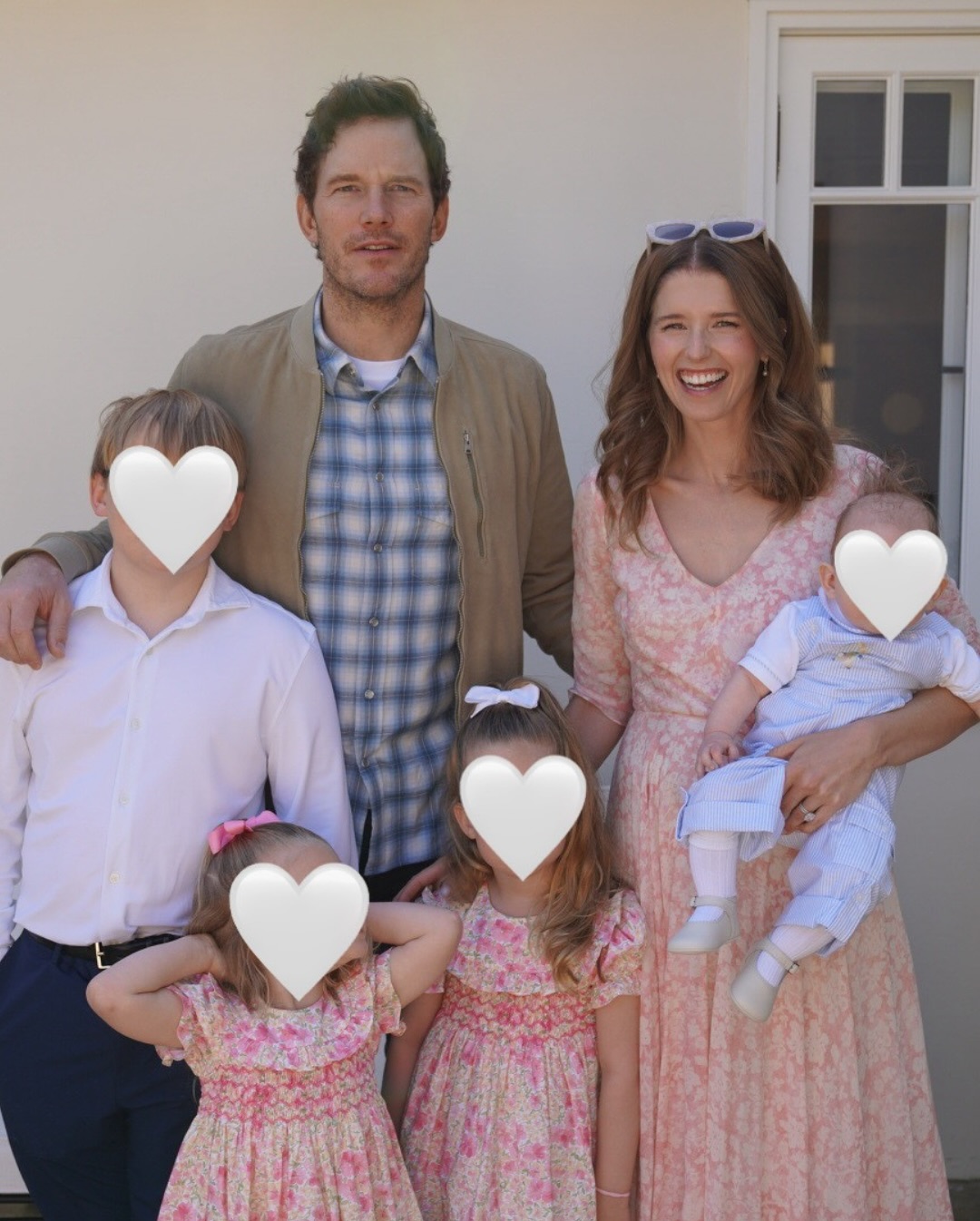 Chris Pratt and Katherine Schwarzenegger posing with their three children, whose faces are obscured by white heart emojis.