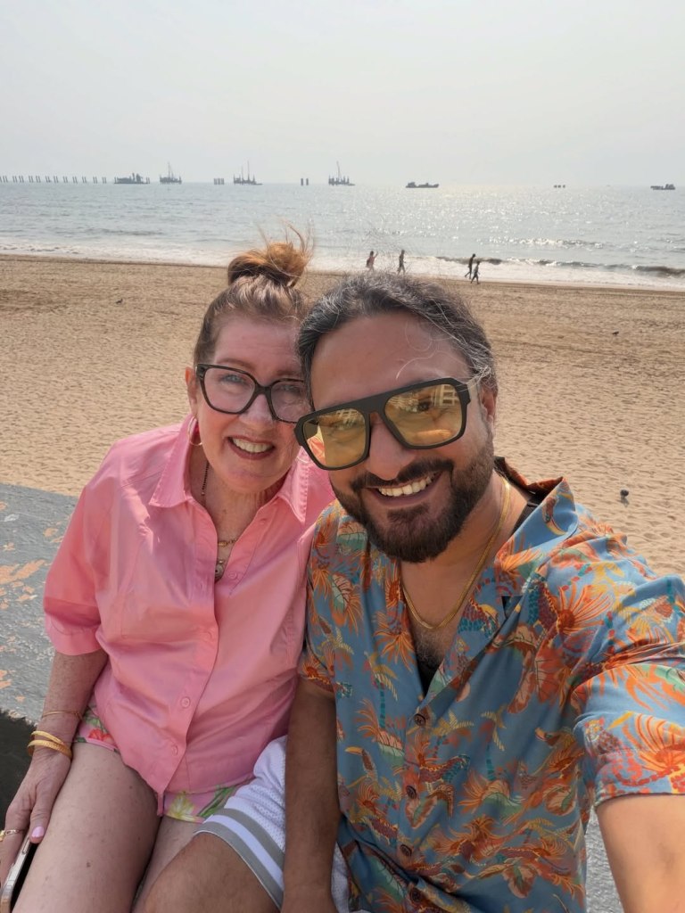 Jenny Slatten and Sumit Singh smiling for a selfie on a beach.