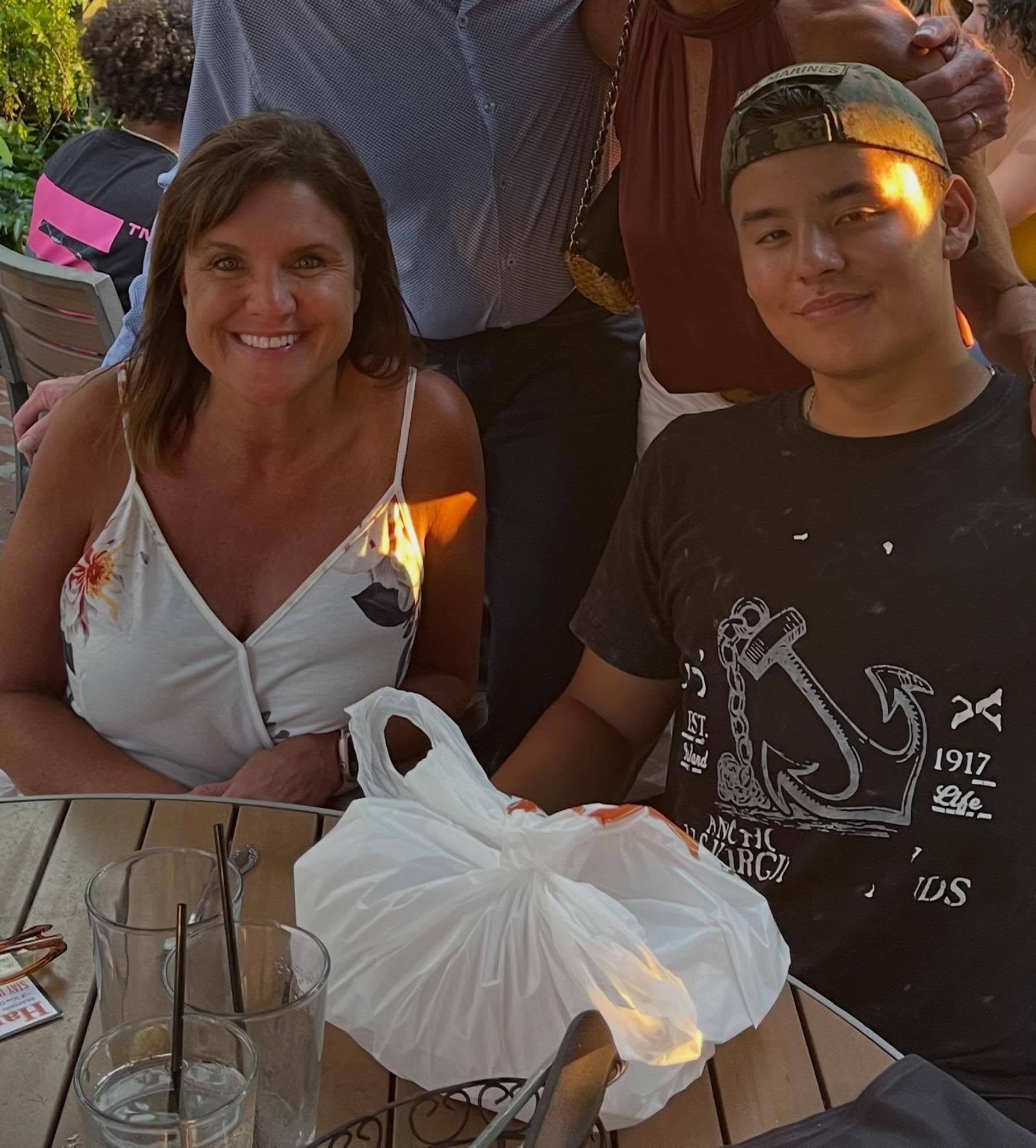 A woman in a floral top and a Collin Gosselin in a black T-shirt and baseball cap sitting at an outdoor table.