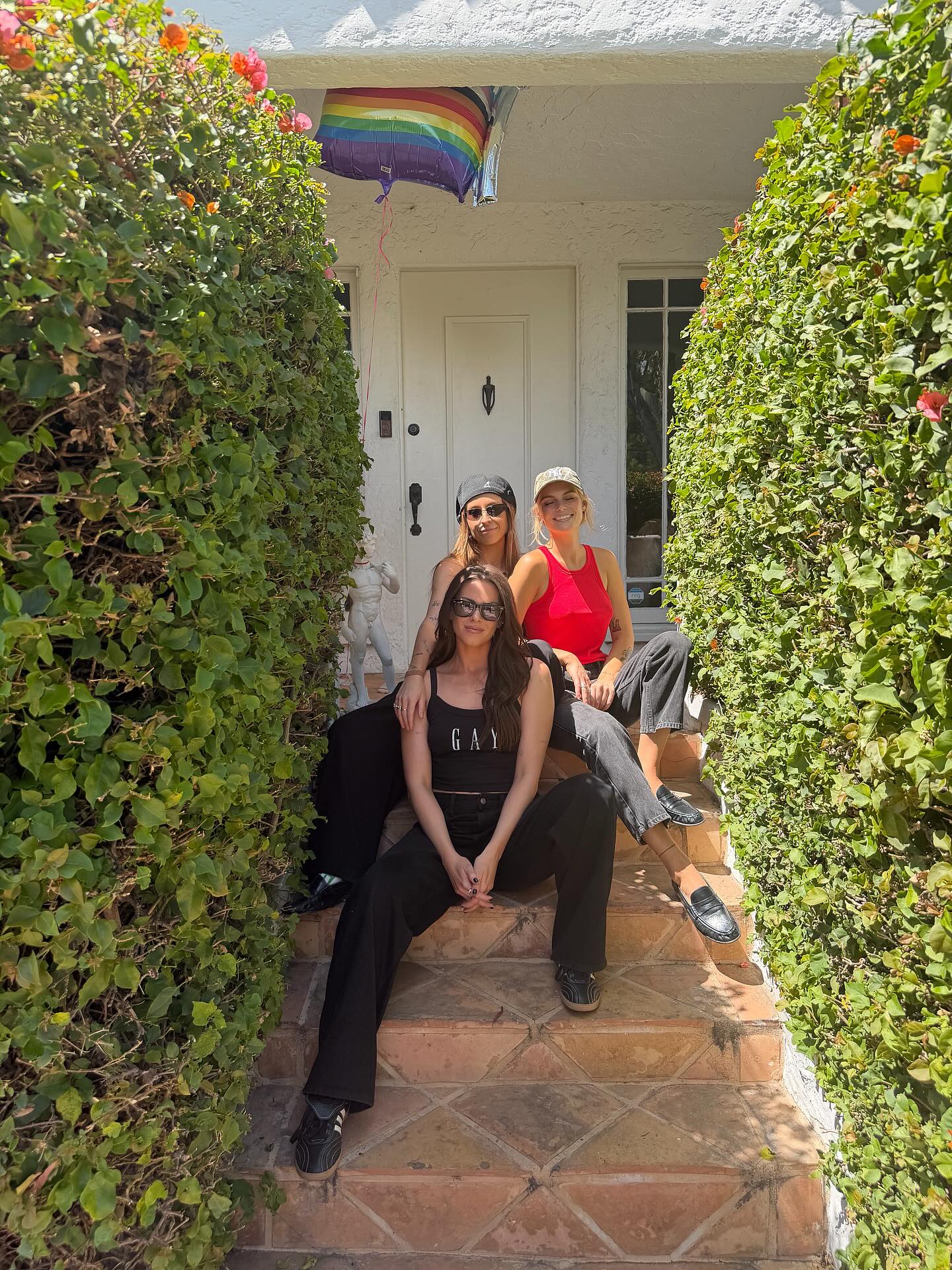 Dayna Kathan with two other women sitting on steps, with a rainbow balloon tied to the door in the background.