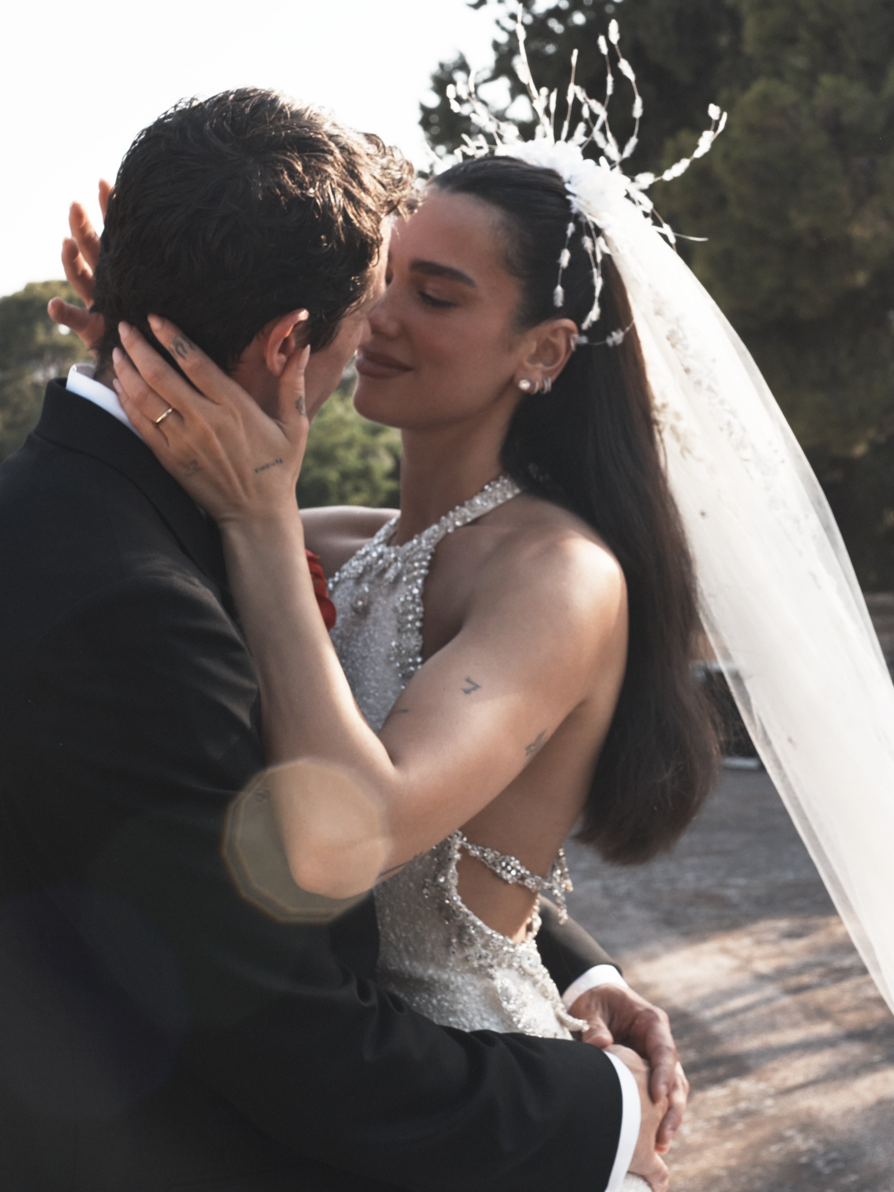 Dua Lipa in a wedding dress embracing a man in a tuxedo.
