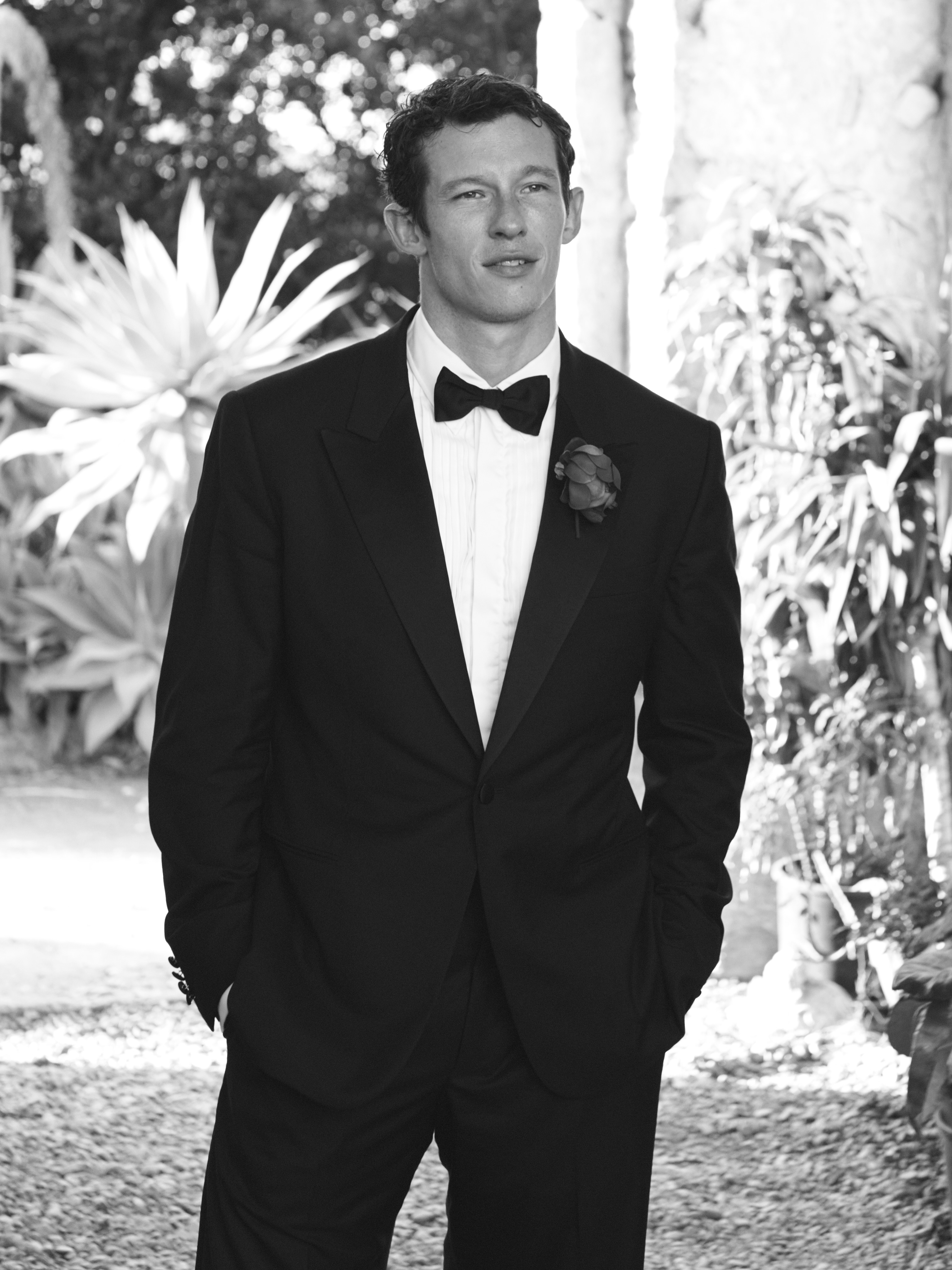 Man in a tuxedo with a boutonnière, standing outdoors.