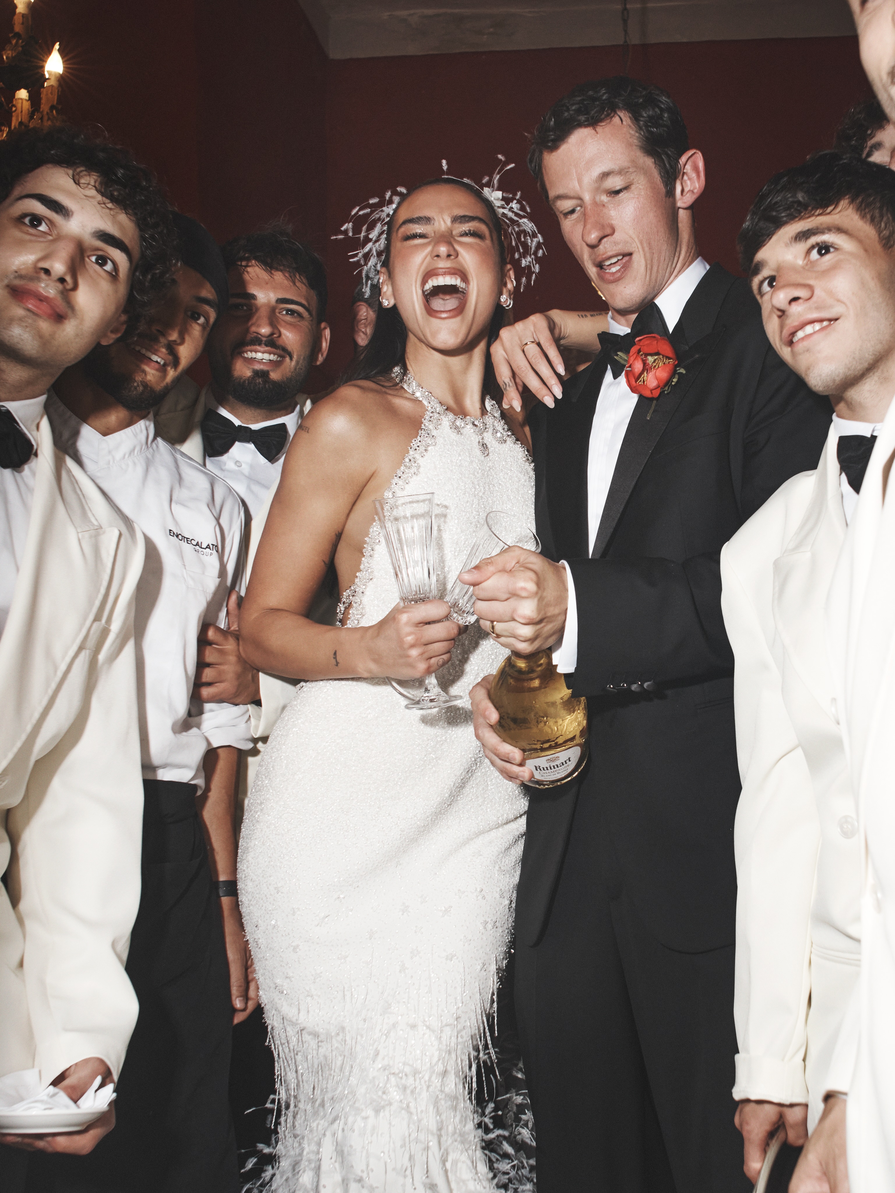 Dua Lipa and a man pop champagne at a wedding.