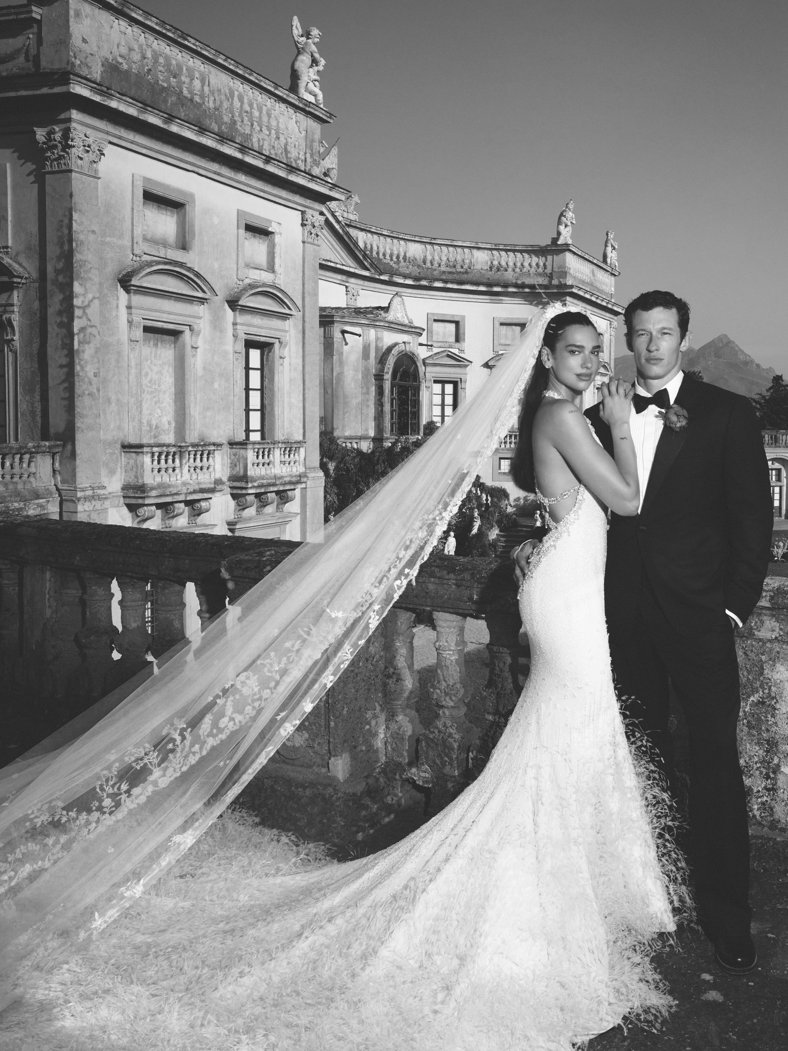 Dua Lipa and a man posing for a wedding photo in front of a grand building.