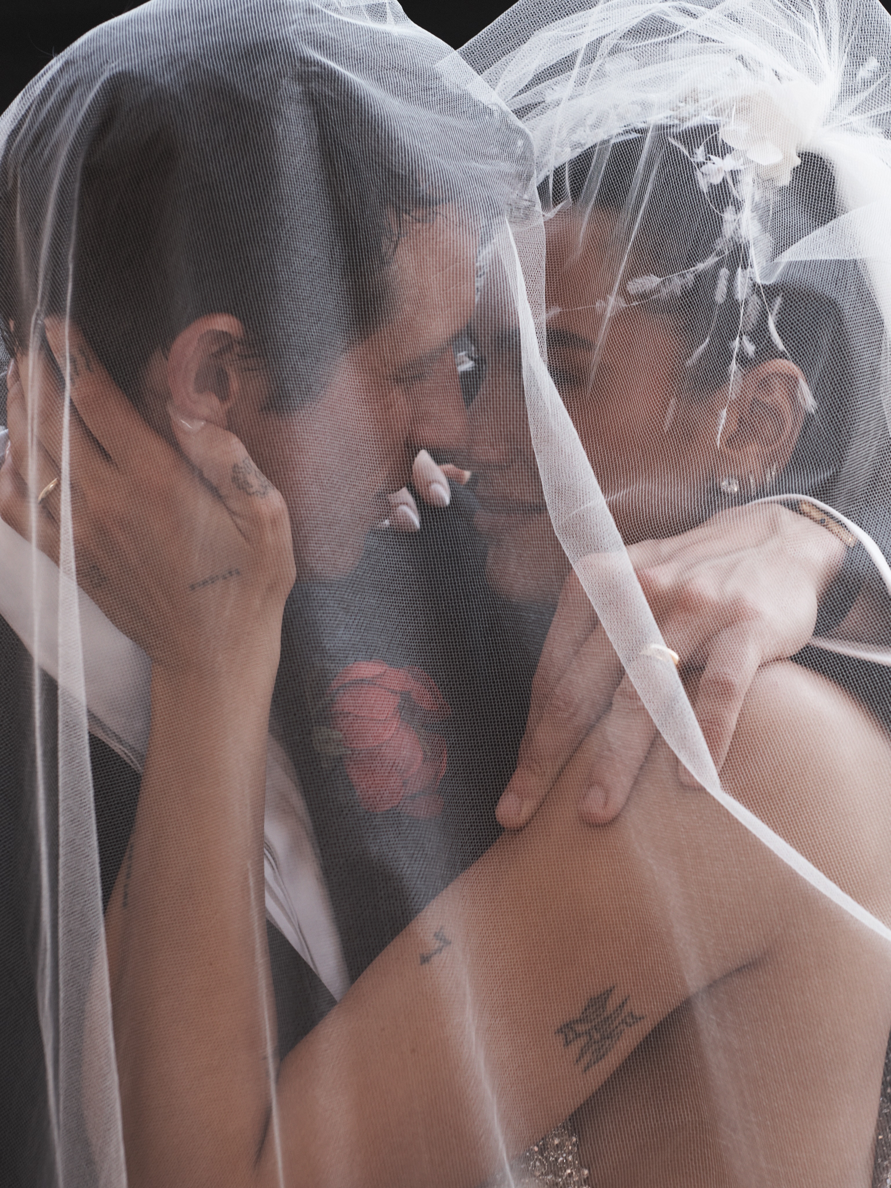 Dua Lipa and Callum Turner embracing under a wedding veil.