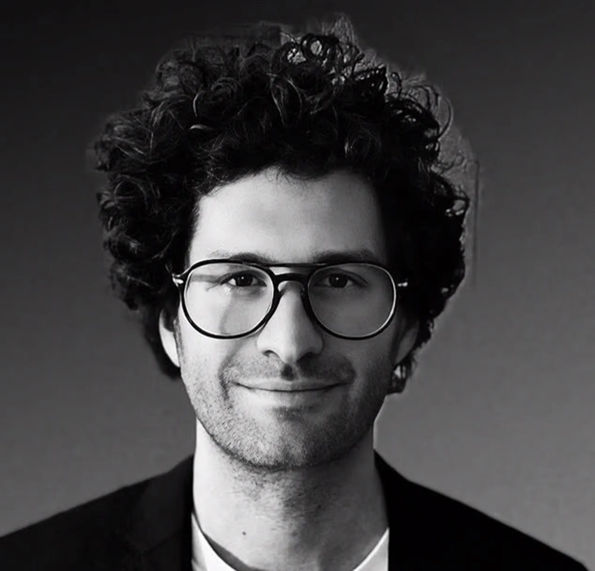 Black and white headshot of Austin Sosa, a man with curly hair, glasses, and a subtle smile.
