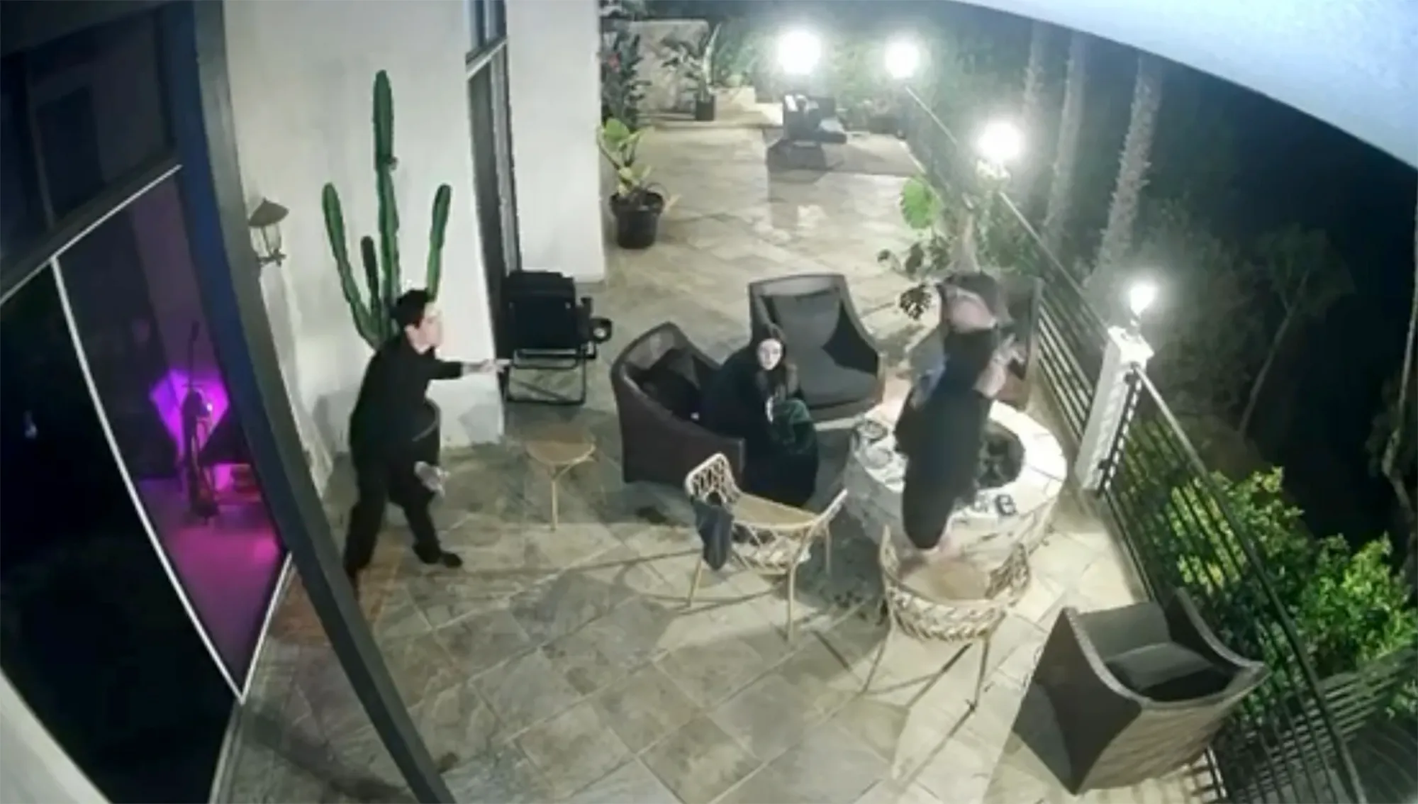 A man in black pushing another man backwards into a lit fire pit.