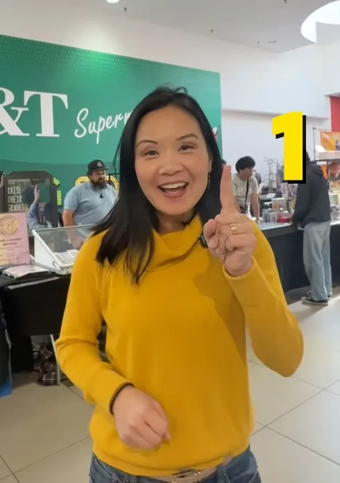 A woman in a yellow sweater smiles and holds up one finger, with a large yellow 