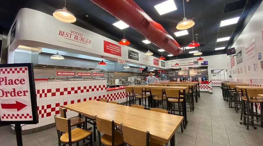 Interior of a Five Guys restaurant with red and white checkered walls, wooden tables, and a 