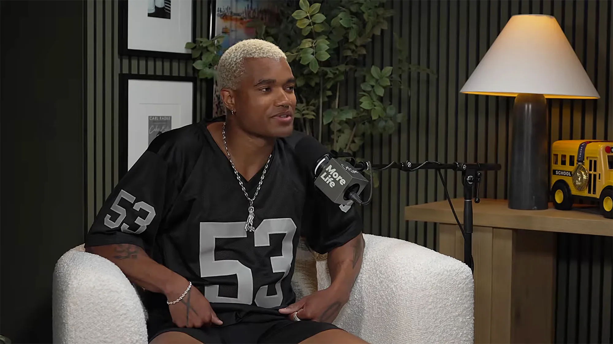 KJ Dillard in a black jersey and silver chain sitting in a white chair.