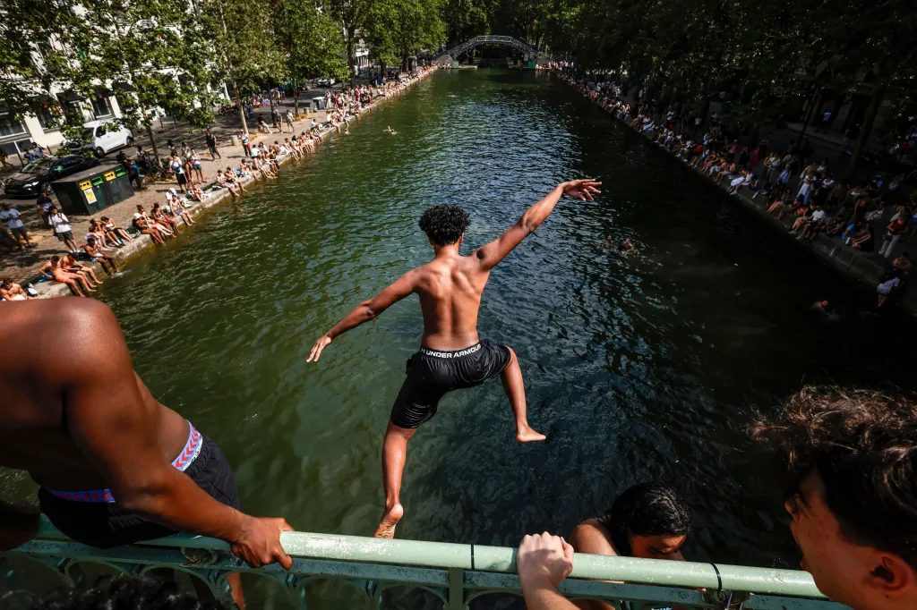 A young man jumping from a bridge into the Canal Saint-Martin to cool off during a heatwave in Paris, France.