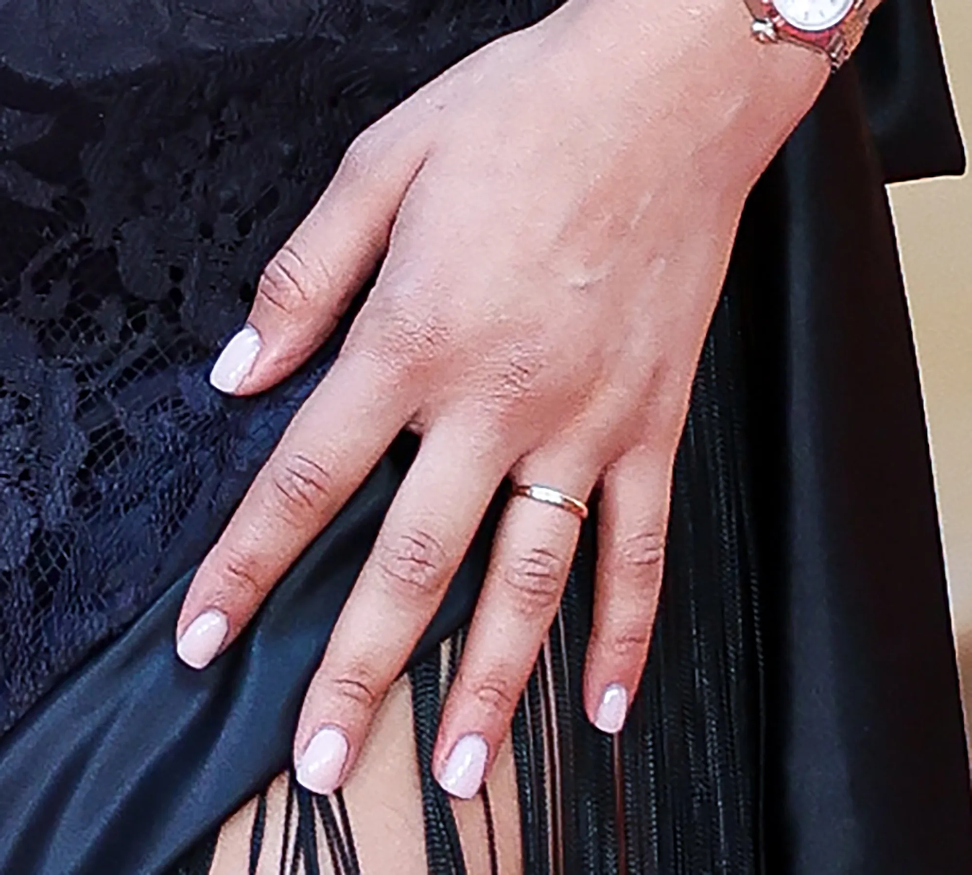 Zendaya's hand with light pink manicured nails, a gold ring, and a watch.