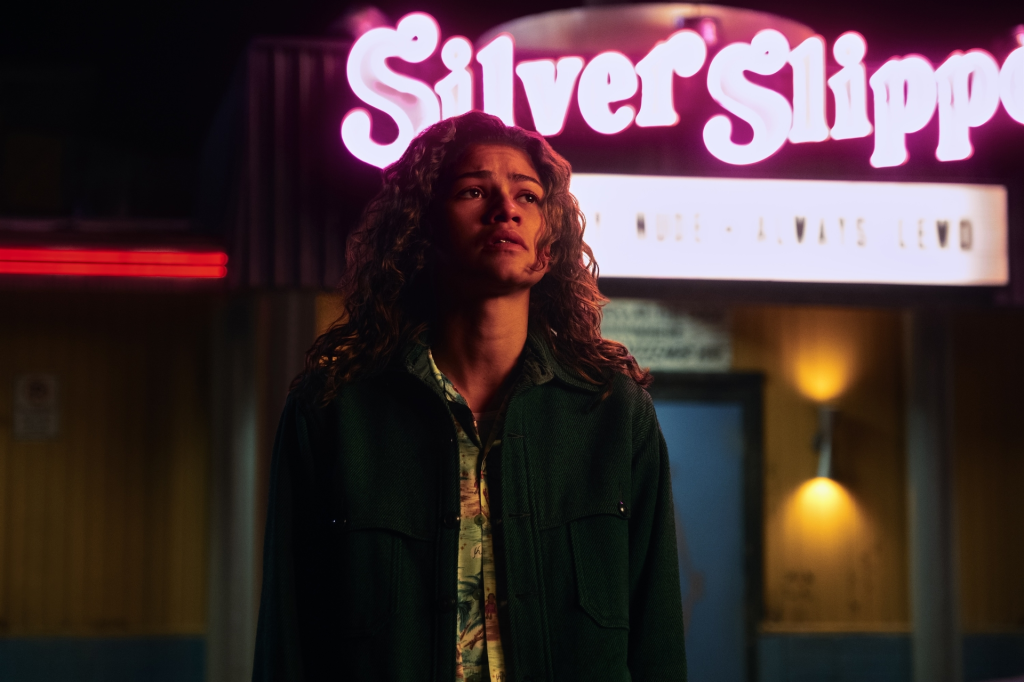 Zendaya as Rue in Euphoria Season 3 standing in front of a neon sign.