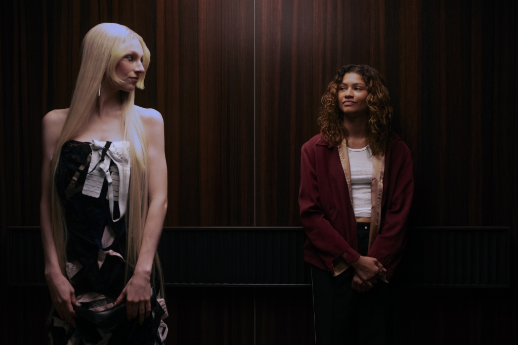 Two women in an elevator, one in a strapless dress and the other in a red jacket and white top.