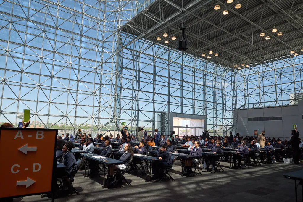 Students taking an exam in a large hall with glass walls.